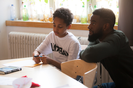 En pojke och en man sitter vid ett bord och arbetar tillsammans med papper och penna i ett ljust rum.
