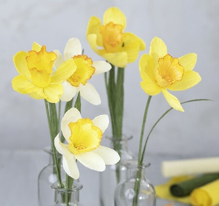 Fyra konstgjorda påskliljor i glasvaser, gjorda av färgat papper i gult och vitt.