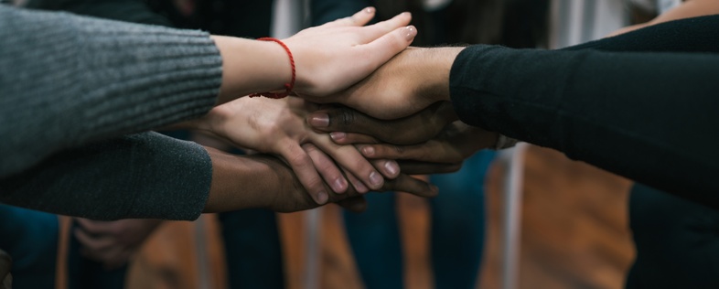 En grupp människor sitter i en cirkel och lägger sina händer ovanpå varandra i mitten som en symbol för samarbete.