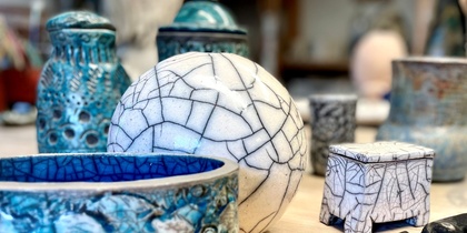 Keramikföremål i blått och vitt står på ett bord tillsammans med en tång i en verkstadsmiljö.