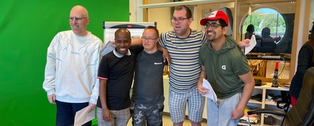 Fem personer står tillsammans och poserar framför en grön skärm i ett kontorsrum.