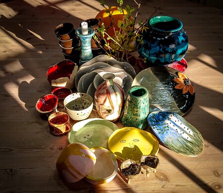 En samling färgglada keramikskålar, fat och vaser står på ett trägolv i solljus.