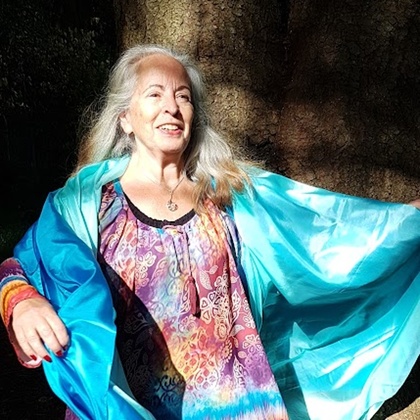 Cirkelledare Elisabeth Hjulström med långt grått hår står barfota utomhus, bär färgglad tunika och blå sjal.