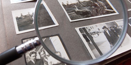 Ett fotoalbum med svartvita fotografier granskas med ett förstoringsglas.