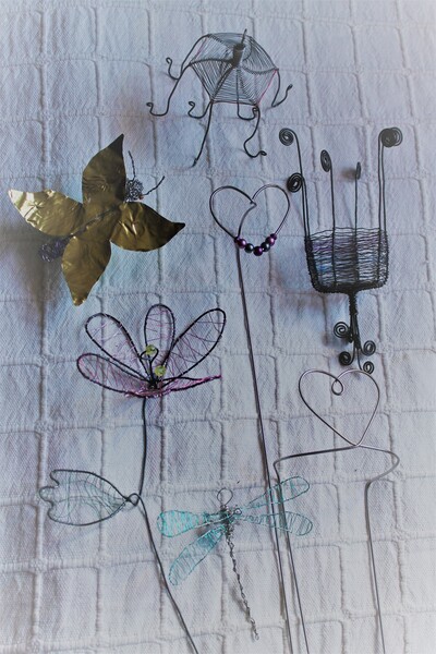 Konstnärliga figurer av metalltråd och papper föreställande blommor, hjärtan, en fjäril och en trollslända mot vit bakgrund.