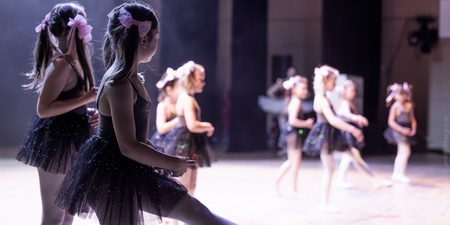 Flera unga flickor i svarta balettklänningar dansar på en scen med mjukt ljus.
