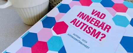 En kopp, en filt och en bok med titeln 'Vad innebär autism?' ligger på en soffa.