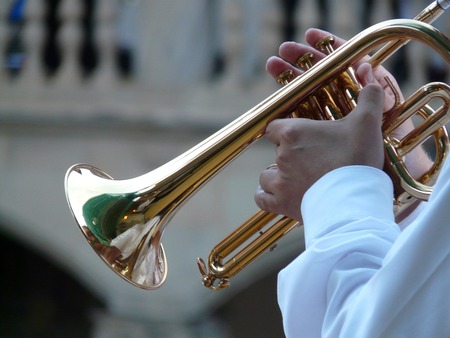 En person i vit skjorta spelar trumpet utomhus, fokus på händer och instrument.