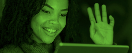 Kvinna med lockigt hår vinkar och ler mot en surfplatta, bilden har ett grönt filter.