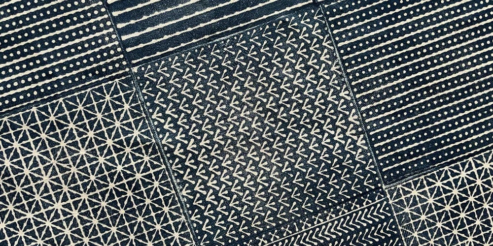 Ett mörkblått och vitt tyg indelat i rutor med olika handtryckta geometriska mönster i japanskinspirerad stil