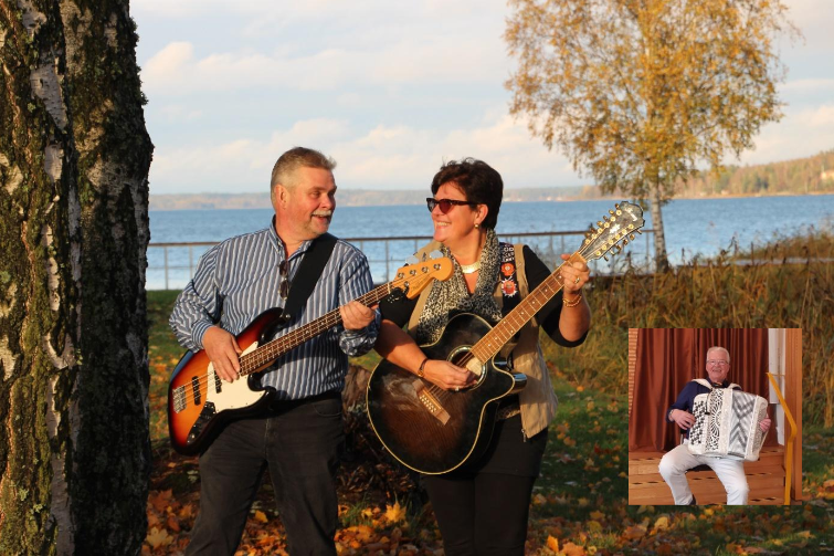 Två personer spelar gitarr och elbas utomhus vid en sjö på hösten, med ett litet foto av en dragspelare infällt.