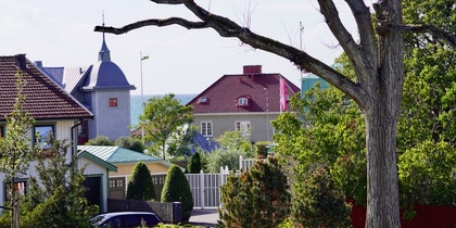Vy över ett bostadsområde med färgglada hus, trädgårdar och ett stort träd i förgrunden.