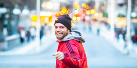 Person i röd jacka och svart mössa står på en stadsgata med suddig bakgrund och ljusprickar.