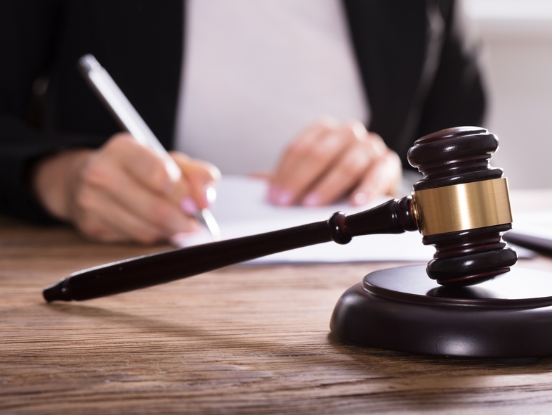 En domarklubba ligger på ett skrivbord medan en person skriver på papper i bakgrunden.