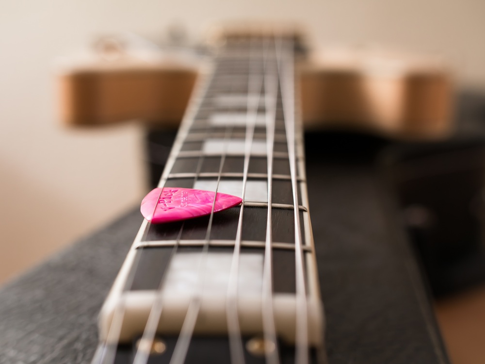 Närbild av en gitarrhals med ett rosa plektrum liggande på strängarna.