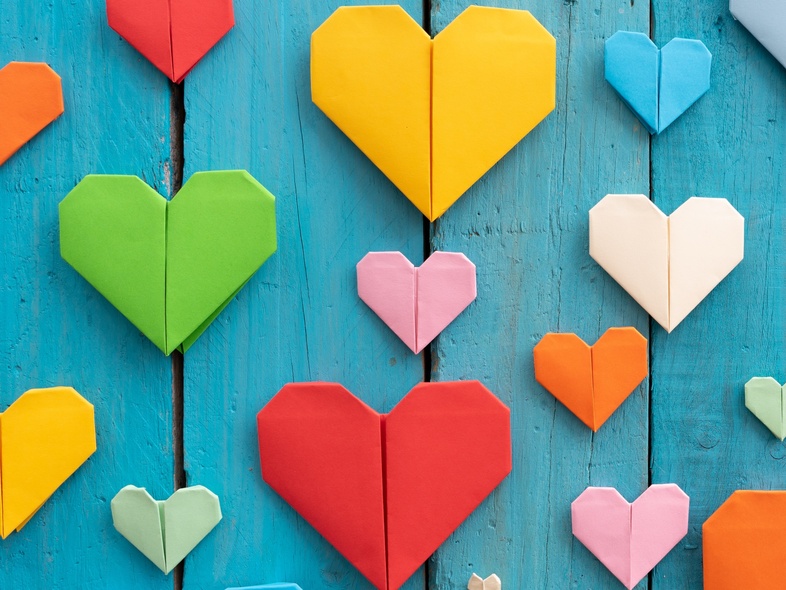 Flera färgglada origamihjärtan i olika storlekar på en blå träbakgrund.