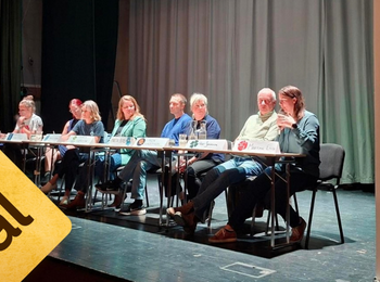 Panel med åtta personer sitter på scen, en person står bredvid. Skylt med texten 'Mitt val' och roll-up från Studieförbundet Vuxenskolan.
