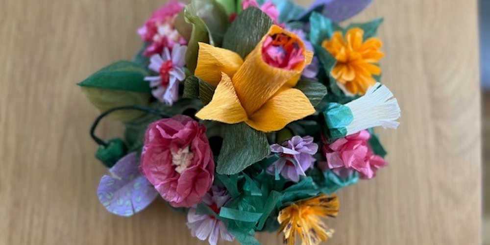 En bukett färgglada pappersblommor står på ett trägolv.
