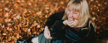 Person sitter på marken bland höstlöv med mörka kläder och svarta skor.