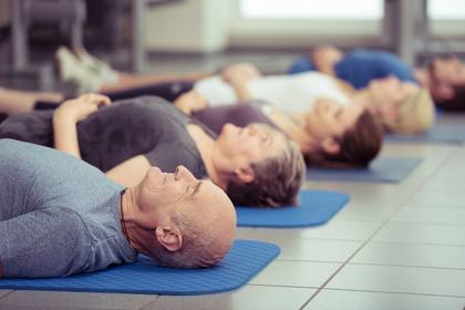 Flera personer ligger på rygg på yogamattor i ett ljust träningsrum.