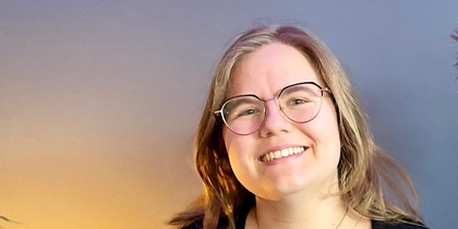 Två leende personer sitter tillsammans i en blå soffa i ett rum med blå vägg och grön växt.