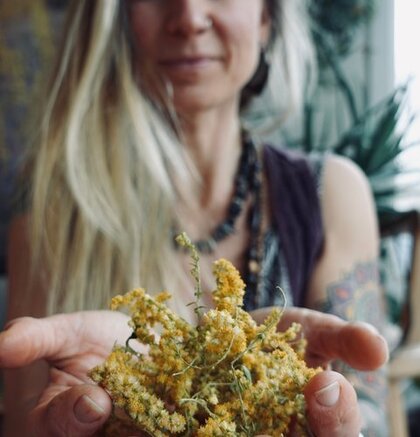 En person håller en bukett med gula torkade blommor i händerna, med tatuering synlig på armen.