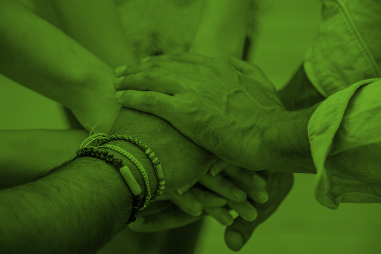 Flera händer lagda ovanpå varandra i en gest av samarbete, bilden har ett grönt färgfilter.