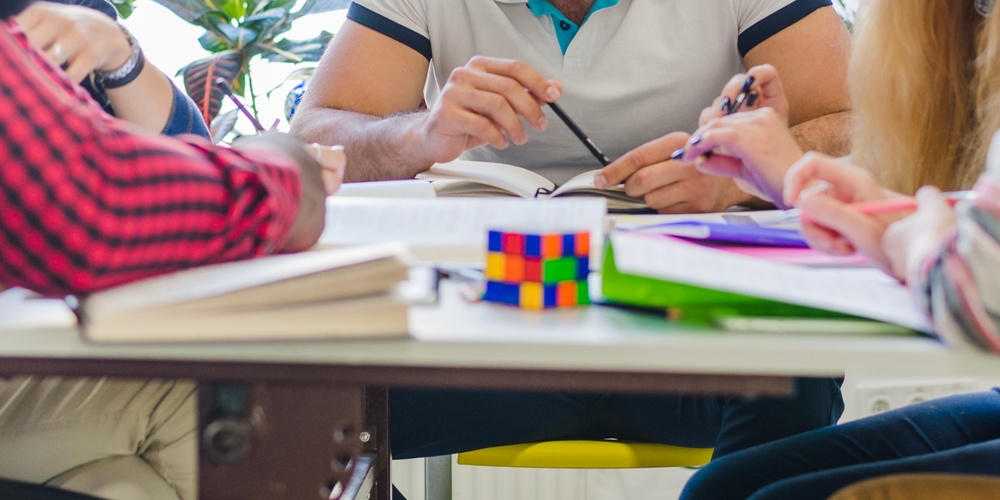 Fem unga vuxna sitter runt ett bord och diskuterar tillsammans i ett ljust rum.
