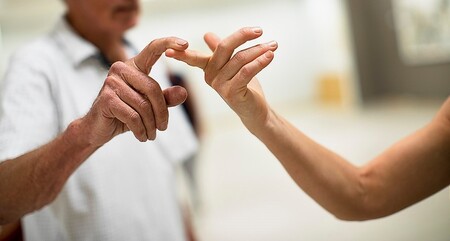 Två personer rör vid varandras fingertoppar i en ljus inomhusmiljö.