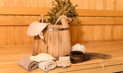 Bastuinteriör med träspann, björkris, handdukar och bastutillbehör på en träbänk.