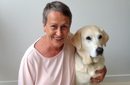 Charlotte Swanstein sitter leende bredvid en ljus labrador och håller armen runt hunden.