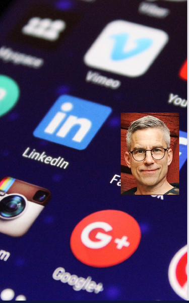 Närbild av mobilskärm med sociala medieappar och ett porträtt av en man med glasögon infällt.