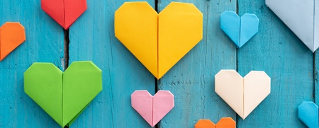 Flera färgglada origamihjärtan i olika storlekar på en blå träbakgrund.
