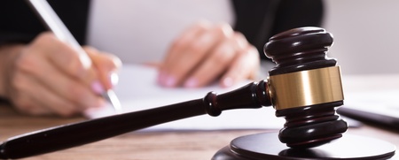 En domarklubba ligger på ett skrivbord medan en person skriver på papper i bakgrunden.