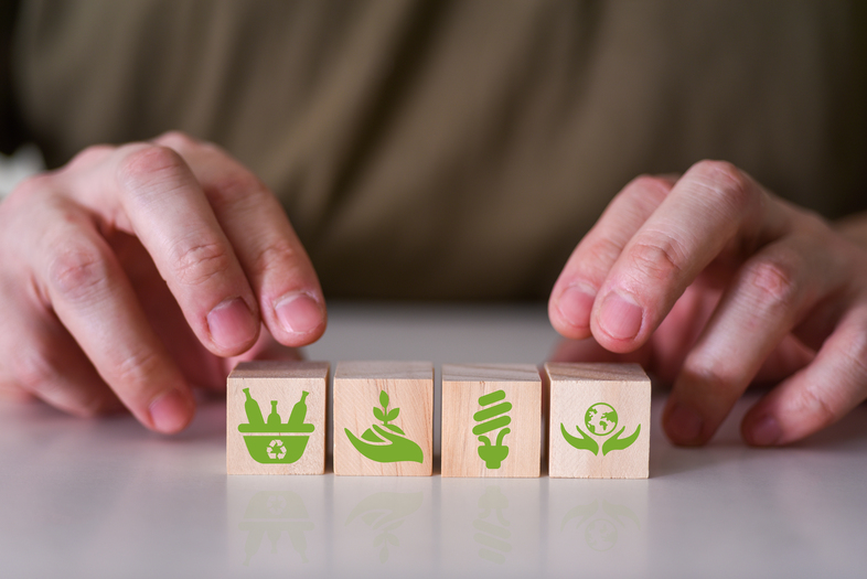 Två händer placerar träklossar med gröna miljöikoner på ett bord.