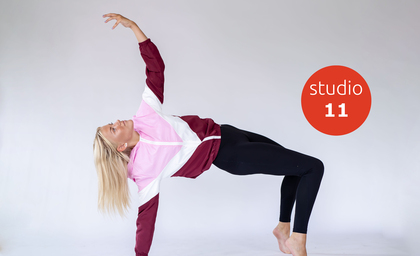 Kvinna i sportkläder gör en yogaposition på golvet med en arm uppsträckt, vit bakgrund, röd cirkel med texten 'studio 11'.