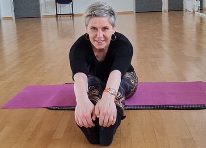 Person sitter på en yogamatta och gör en framåtböjning i ett ljust träningsrum.