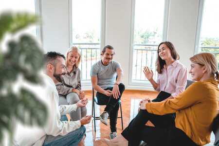 En grupp människor sitter på stolar i en ring och samtalar.