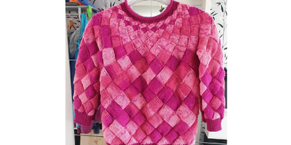 En stickad tröja i rosa och cerise nyanser med rutmönster, hänger på en galge.