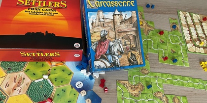 Två sällskapsspel, Settlers från Catan och Carcassonne, uppdukade på ett bord med spelbrickor och pjäser.