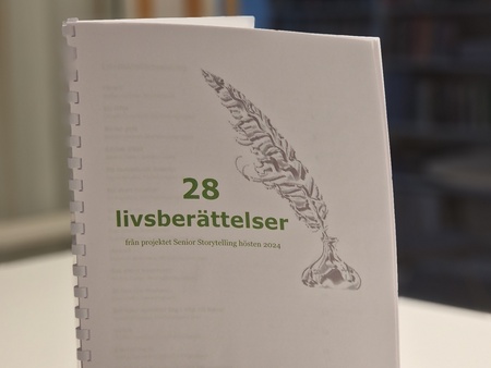 Ett häfte med titeln '28 livsberättelser' står uppställt på ett bord i ett bibliotek.
