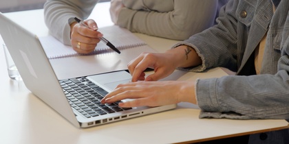 Två personer sitter vid ett bord, en skriver på en laptop och den andra antecknar i ett block.