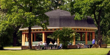 En paviljong i en grön park med människor som sitter vid bänkar och cyklar parkerade bredvid.