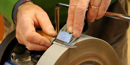 En person slipar ett verktyg mot en roterande slipsten med händerna.