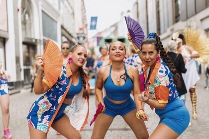 Tre kvinnor i färgglada kläder dansar med solfjädrar på en stadsgata under en festival.