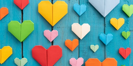 Flera färgglada origamihjärtan i olika storlekar på en blå träbakgrund.