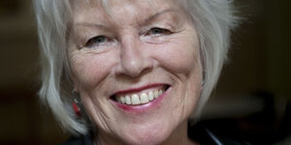 Person med vitt hår, svart läderjacka och halsband står inomhus. Ansiktet är suddat.