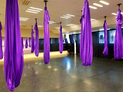 Ett rum med flera lila tyghängmattor upphängda från taket, troligen för aerial yoga eller fitness.