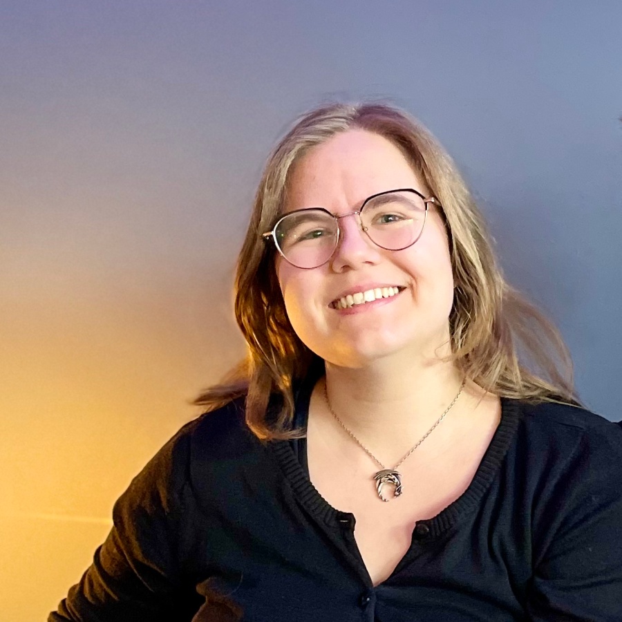 Två leende personer sitter tillsammans i en blå soffa i ett rum med blå vägg och grön växt.