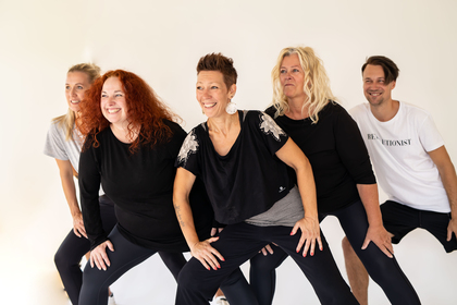 Fem vuxna personer står i en grupp och gör en gemensam träningsövning, alla ser glada ut.